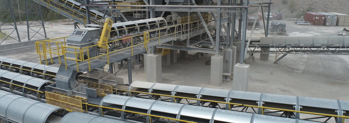 Multiple conveyor lines with galvanized ¾ open-side RPS covers converging at a quarry crushing plant, belts visible along the open sides